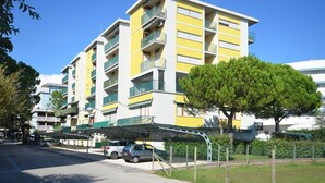 A multi-story residential building with balconies and a covered parking area. - Cozy studio with balcony and sea view (Bibione)