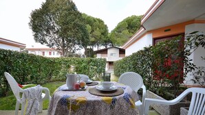 An outdoor dining area with a table set for two, surrounded by white plastic chairs. - Peaceful getaway in a cozy villa (Bibione)