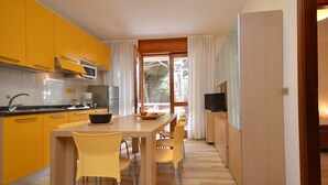 A modern kitchen with yellow cabinets, a dining table with chairs, a large window, and a television.