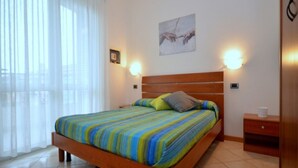 Un dormitorio con una cama de madera, ropa de cama a rayas, una mesita de noche y una lámpara fijada a la pared.