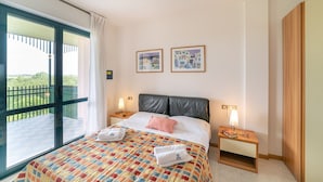 Habitación de hotel con una cama grande, dos mesitas de noche, un armario y un balcón con vistas.