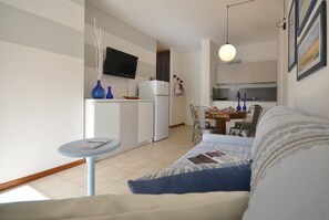 A compact living space with a kitchenette, a dining area, and a sofa with a small side table.
