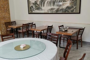 A dining area with wooden tables and chairs, a glass table in the center, and a large painting on the wall.