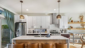 A modern kitchen with white cabinets, a central island with bar stools, stainless steel appliances, and pendant lighting.