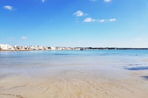 A beach with clear blue water and a cityscape in the background.