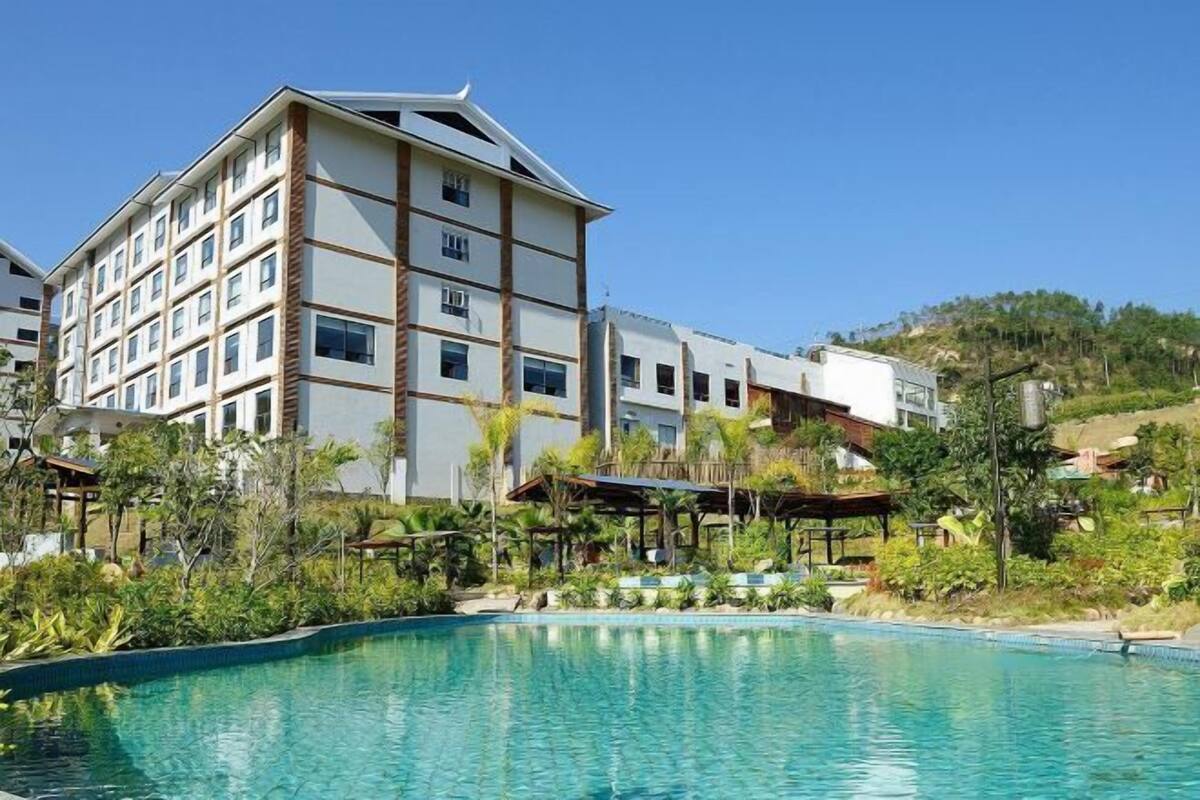 Un hotel de varios pisos con piscina y abundante vegetación.