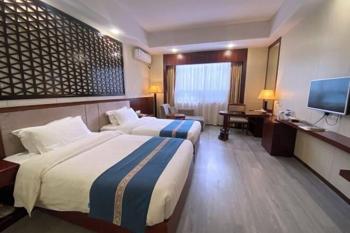 Habitación de hotel con dos camas, un escritorio, un televisor y un panel decorativo en la pared.