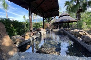 Un área de piscina al aire libre tranquila, con un porche de madera, rodeada de rocas y abundante vegetación.