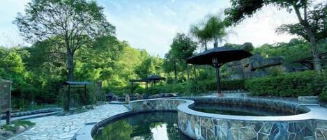 A circular pool with stone edges, surrounded by a stone pathway and lush greenery.