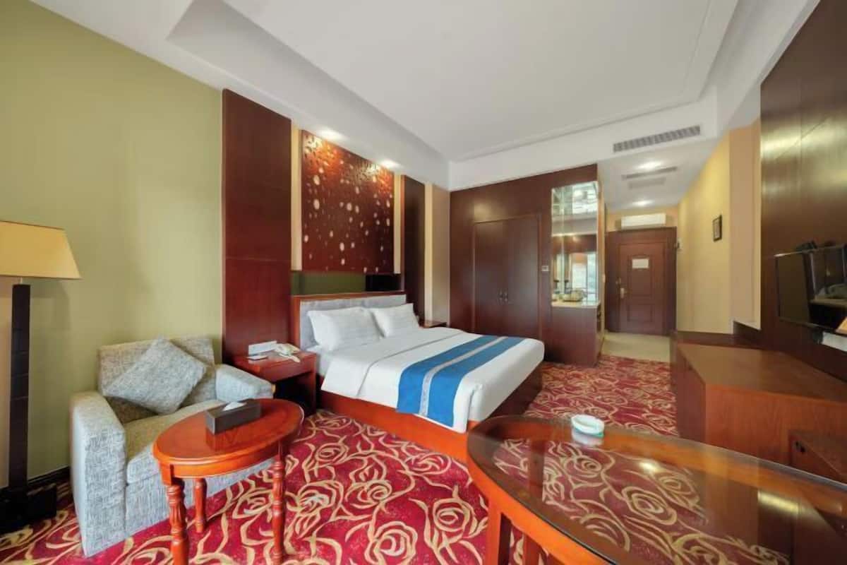 Una habitación de hotel con cama, sofá, una mesita, escritorio y espejo.