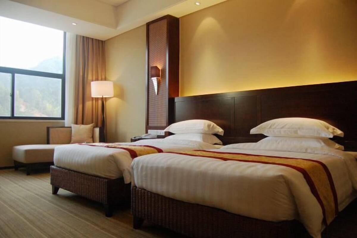 Habitación de hotel con dos camas, un ventanal grande, una lámpara de pared y vistas al exterior.