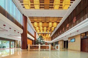 Um hall amplo com teto alto, grandes janelas e uma árvore ornamental central.
