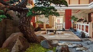 Un intérieur de style japonais traditionnel, agrémenté d’un jardin de rochers, d’un grand arbre et d’un espace détente avec des coussins.
