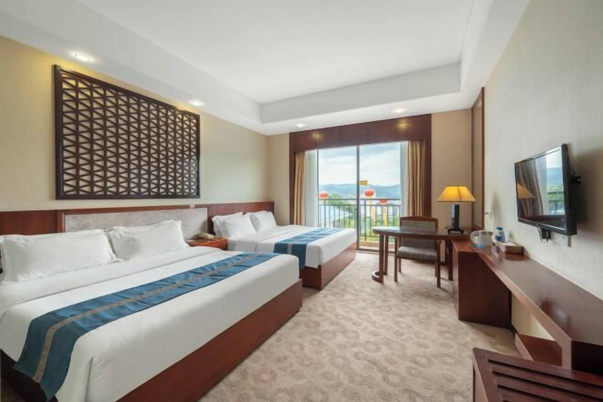 Habitación de hotel con dos camas, televisión, escritorio y balcón con vistas.