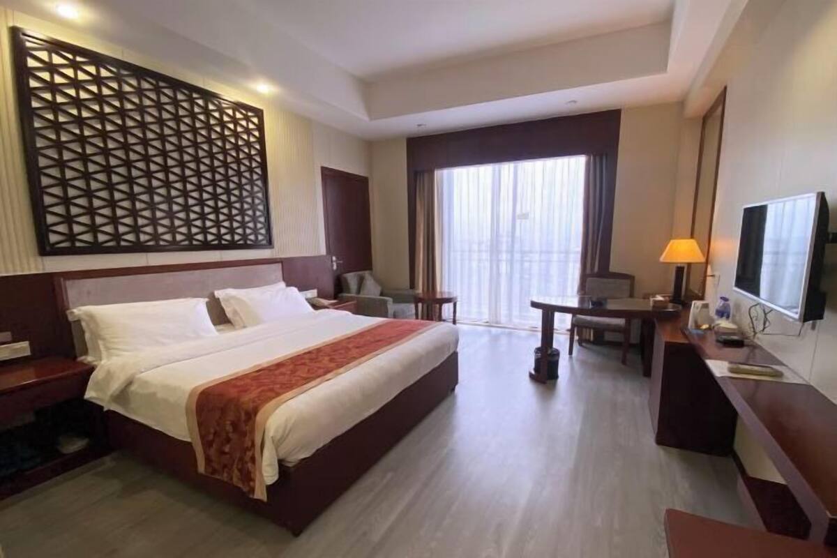 Habitación de hotel con una cama grande, un escritorio, una silla, un televisor y una ventana con cortinas.