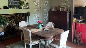 Een eetruimte met een houten tafel, witte stoelen, een kroonluchter en een open haard met een klok aan de muur.