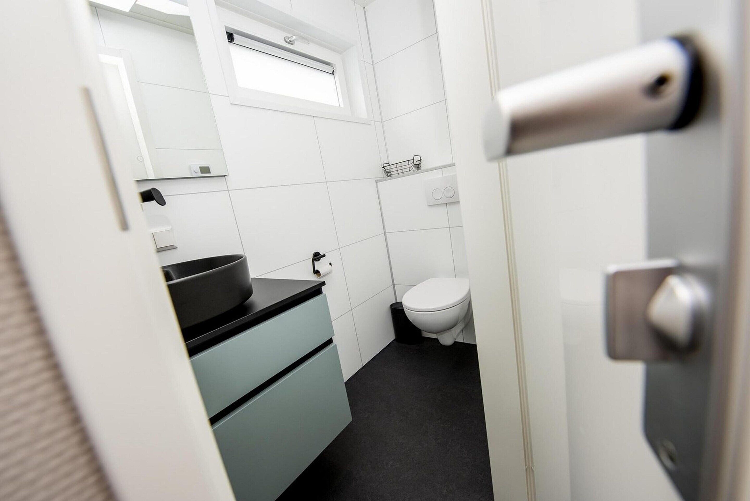 A small, modern bathroom with white tiles, a black countertop, and a white toilet.