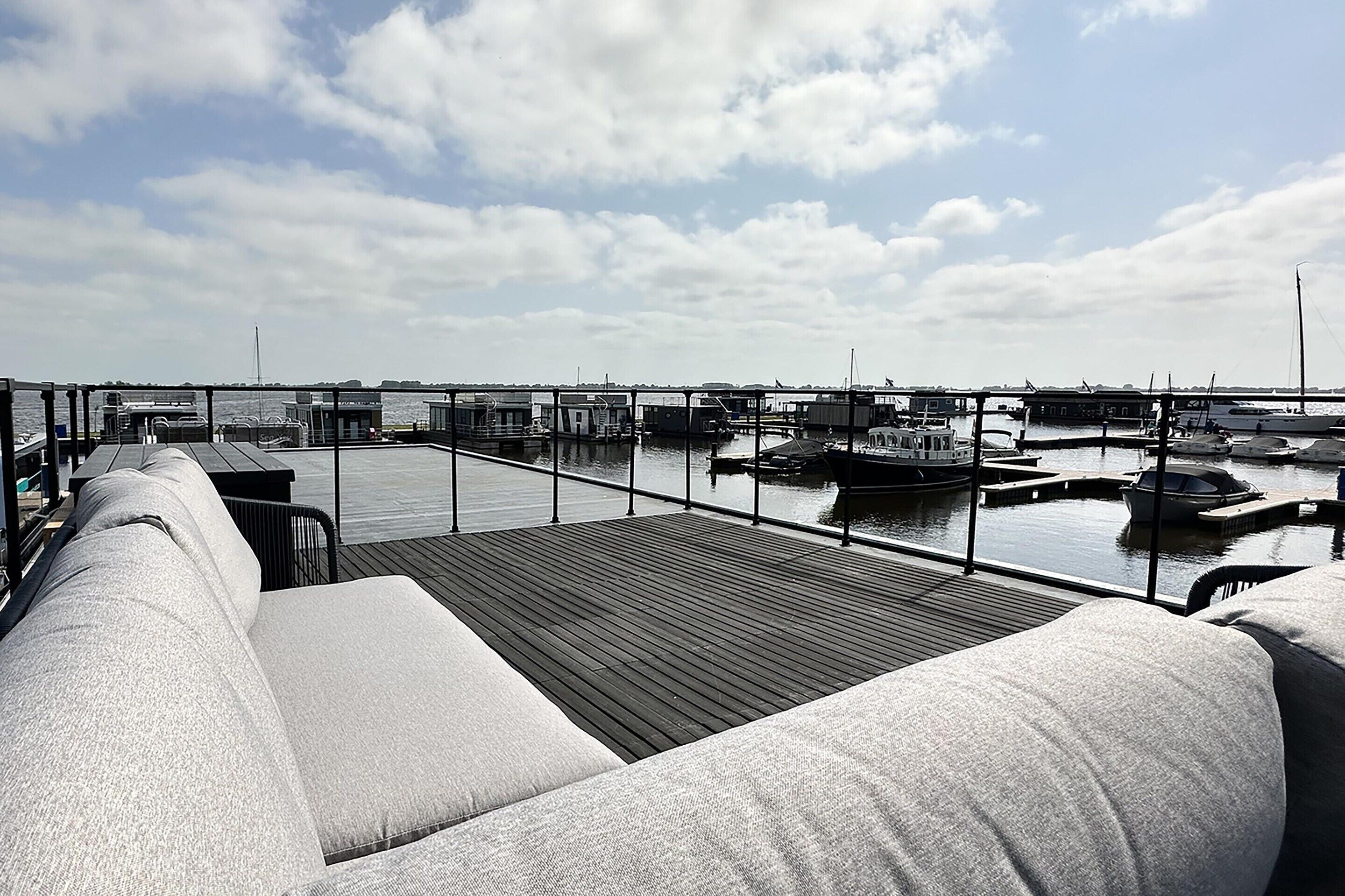 A marina with boats docked, a wooden deck, and a seating area with cushions.
