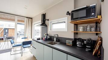A modern kitchen with a built-in microwave, a sink, and a coffee maker. There is a window above the sink and a wooden shelf with glasses.