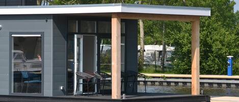 A modern floating structure with a covered deck, glass doors, and outdoor seating.