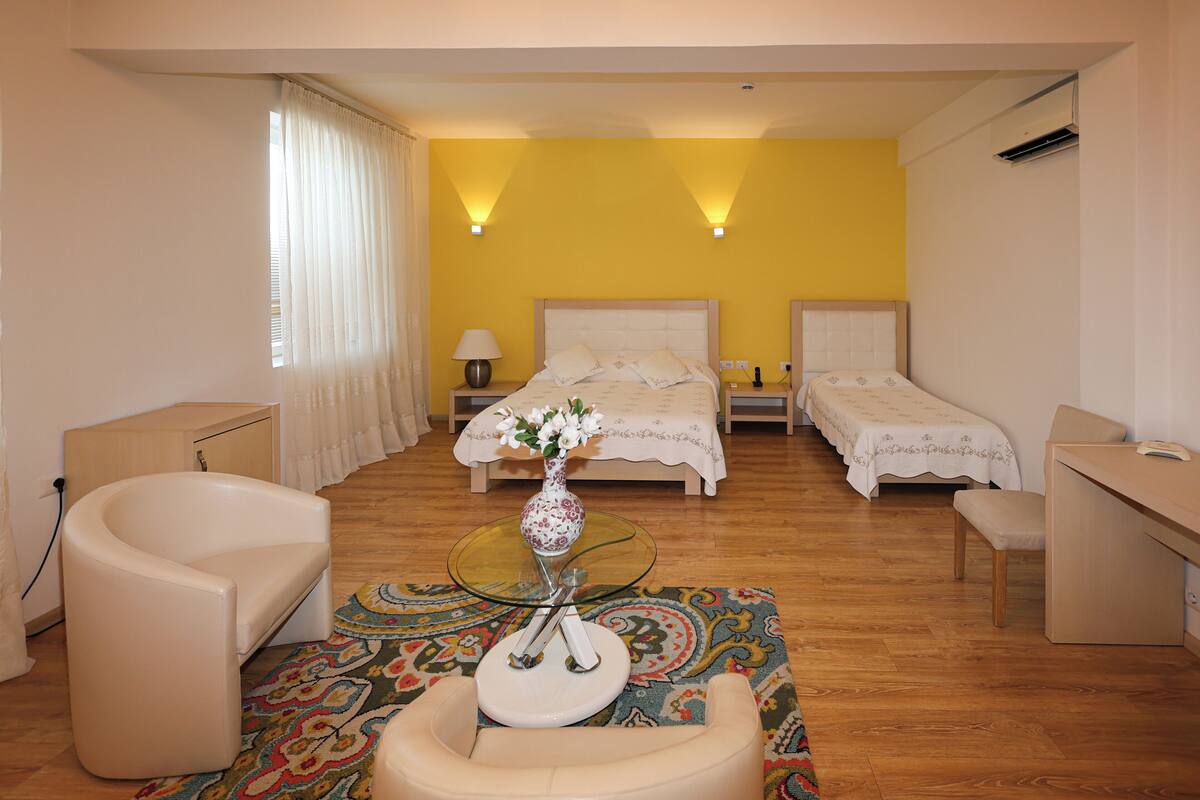 Quarto de hotel com duas camas, área de estar com uma poltrona e uma mesinha, e uma escrivaninha.