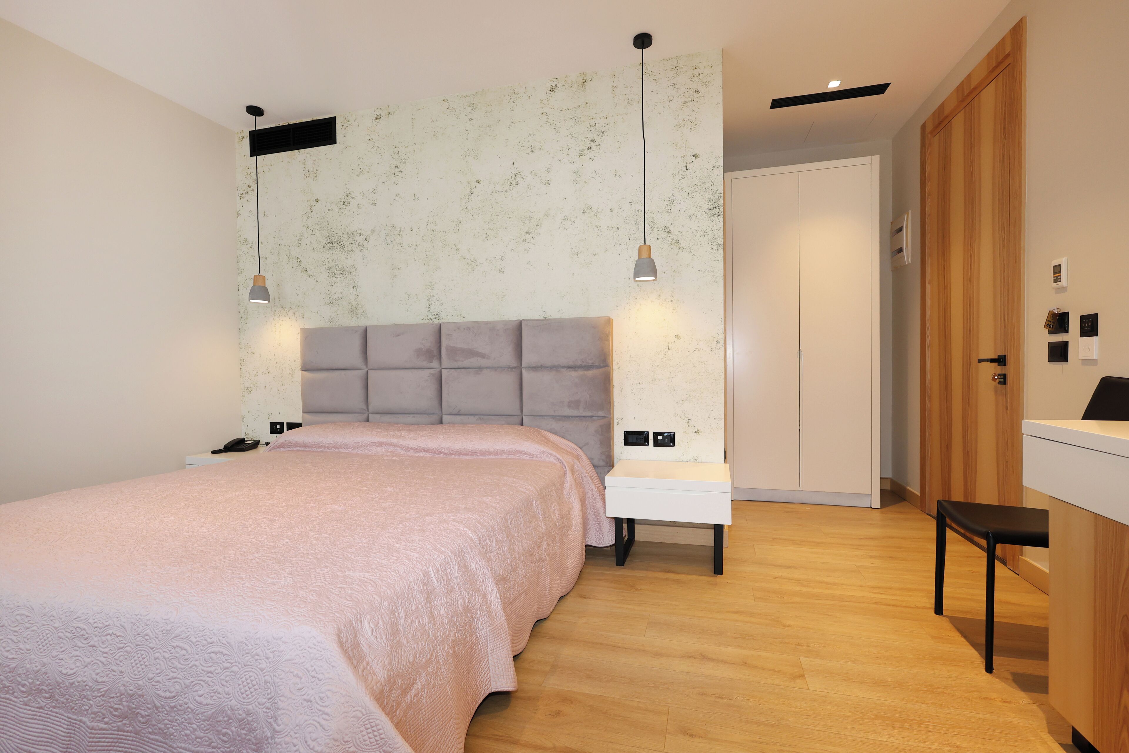 A modern bedroom with a large bed, bedside tables, a wardrobe, and pendant lights.