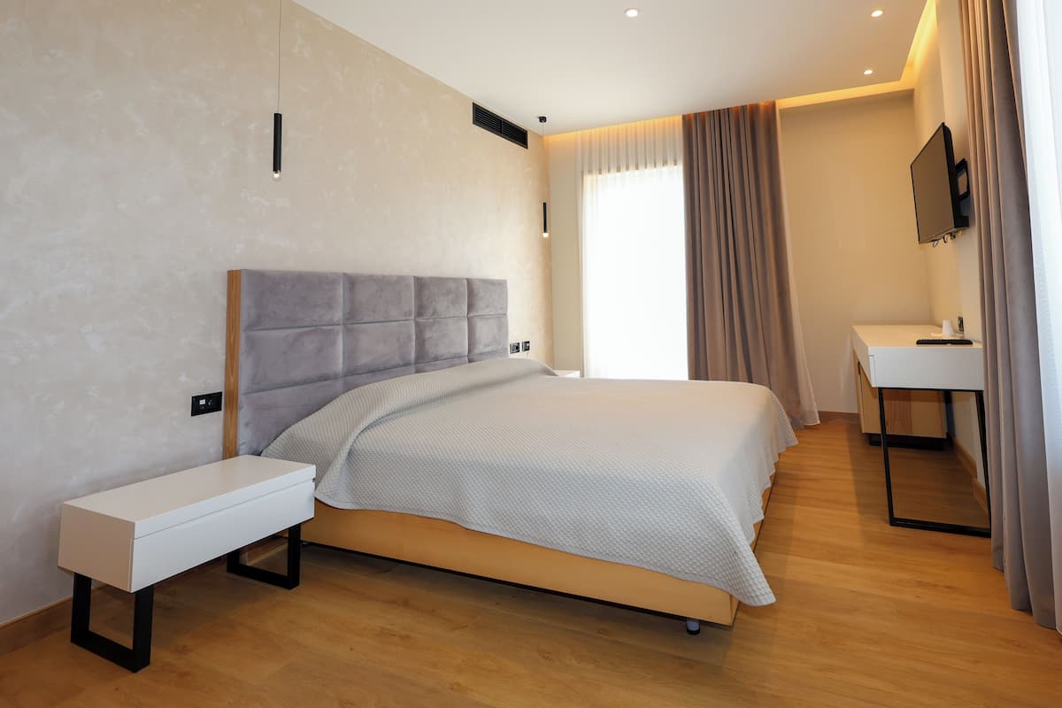 Quarto de hotel moderno com uma cama grande, mesa de cabeceira e pequena escrivaninha com cadeira.