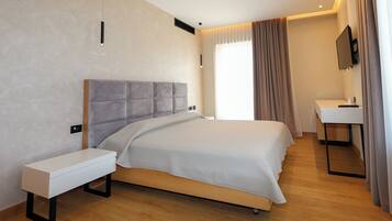 A modern hotel room with a large bed, bedside table, and a small desk with a chair.