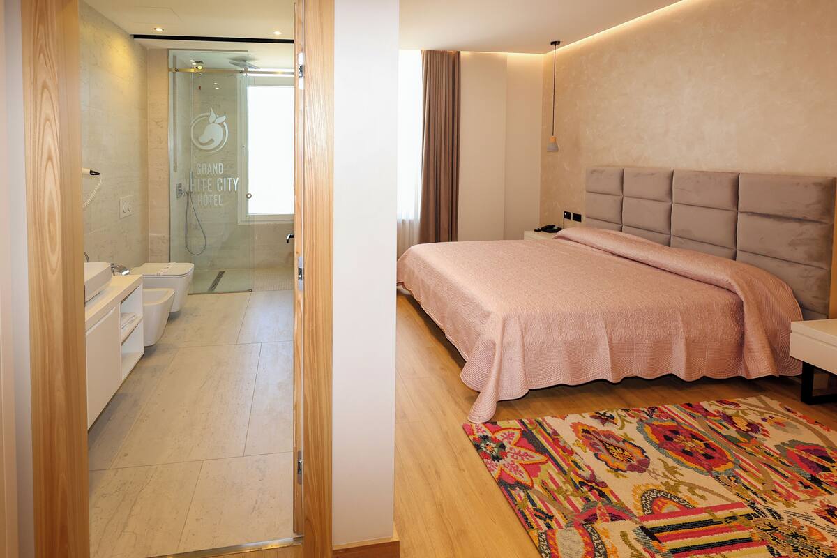 Quarto de hotel com chuveiro, cama com cabeceira, mesa de cabeceira e tapete colorido.