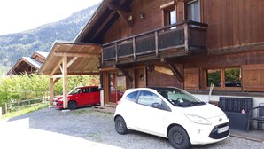 Eine Holzhütte mit überdachtem Carport, ein rotes Auto und ein weißes Auto davor geparkt.