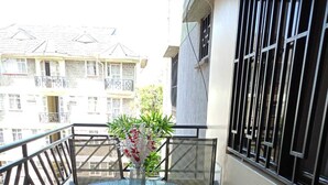 A small outdoor balcony with a round table and four chairs, a potted plant, and a view of buildings in the background. - Lux Suites Narayan Apartments Kisumu (Kisumu)