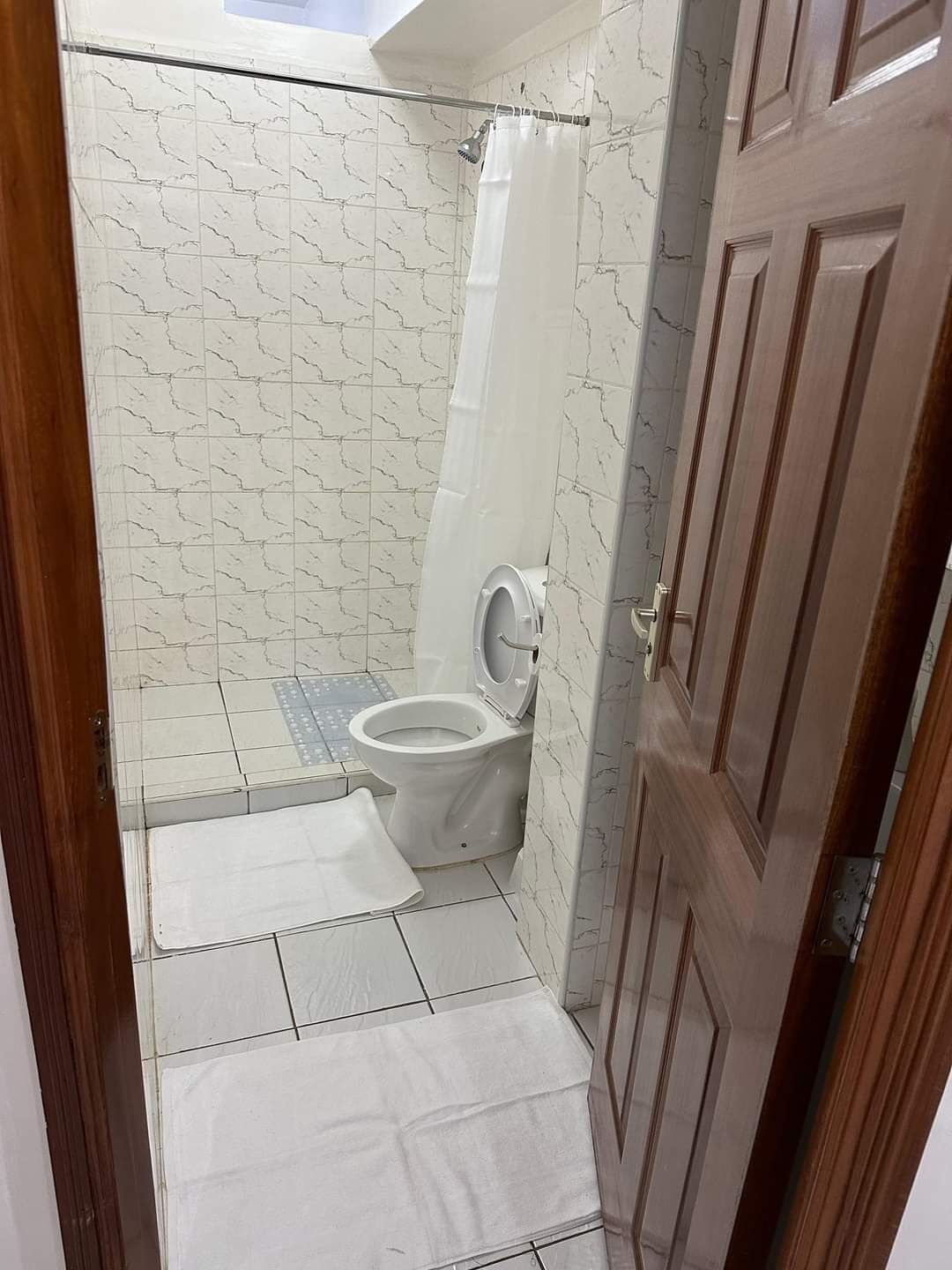A small bathroom with a toilet, a shower curtain, and a tiled floor.