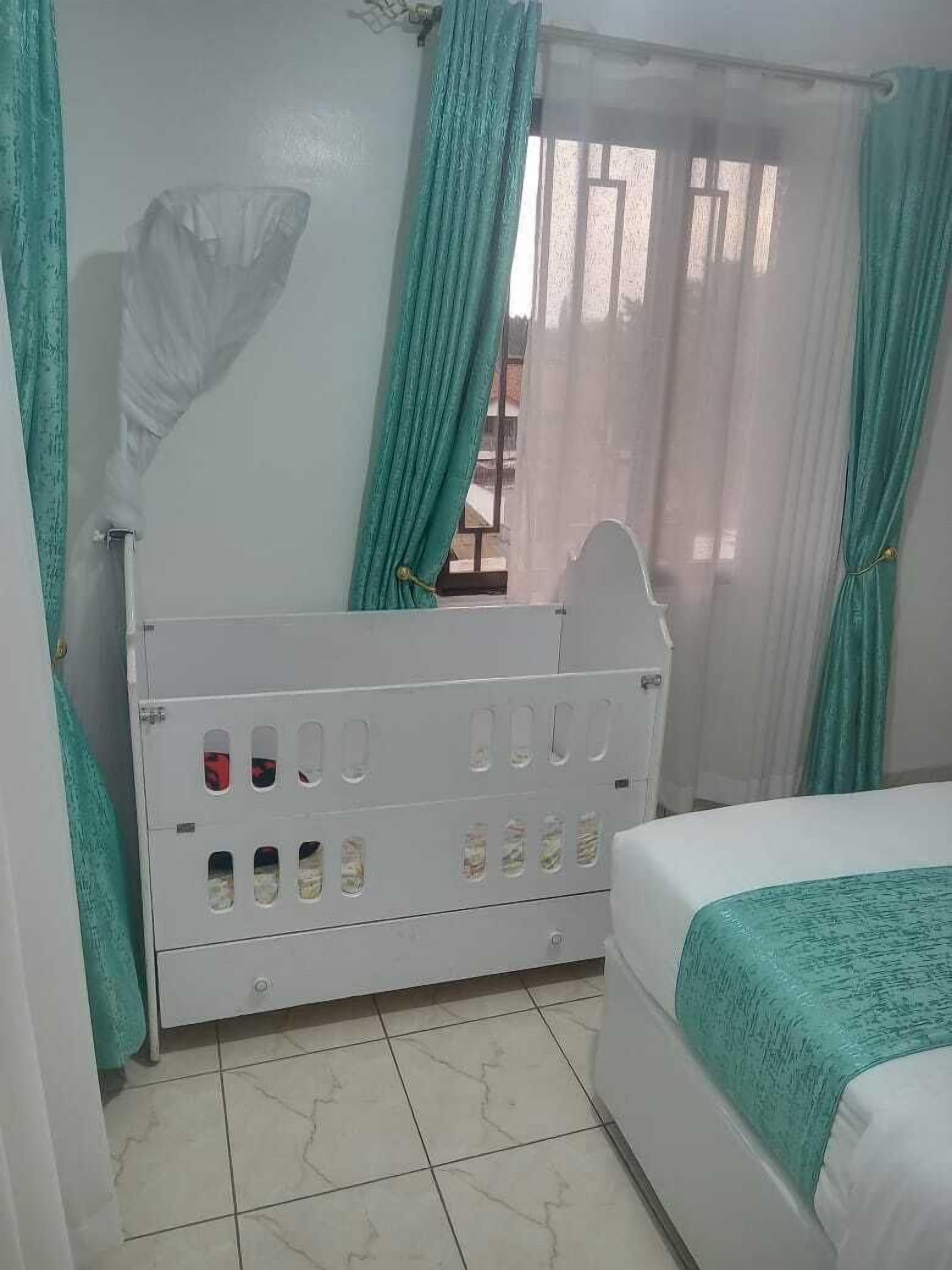 A bedroom with a white bed, a white nightstand, a window with curtains, and a tiled floor.