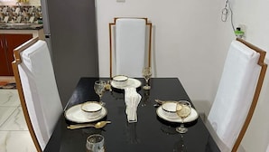 A dining table set for four with white plates, gold cutlery, and a vase centerpiece. - Lux Suites Narayan Apartments Kisumu (Kisumu)
