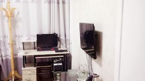 Une pièce comprenant un bureau, un ordinateur, une télévision et une guitare.