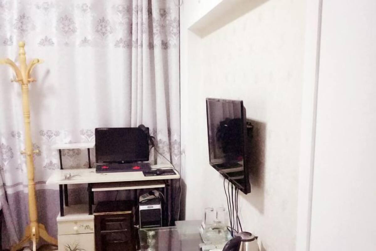 A room with a desk, a computer, a television, and a guitar.