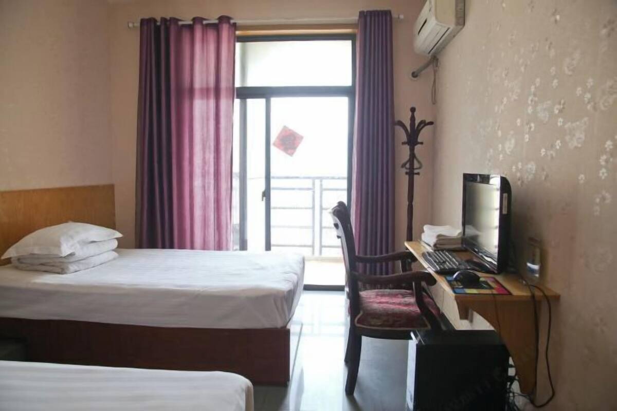 A hotel room with a bed, a desk with a computer, a chair, and a window with curtains.