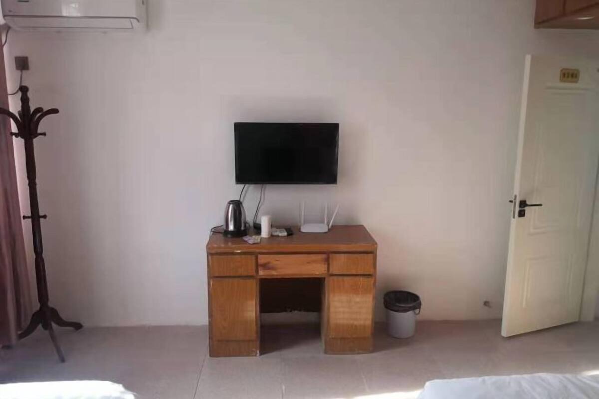 A room with a wooden desk, a flat-screen TV, a white door, and a trash bin.