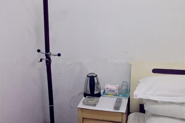 A small room with a bed, a nightstand with a kettle, a remote control, and a box of tissues. - Guangde Sihai Hotel (Guangde)