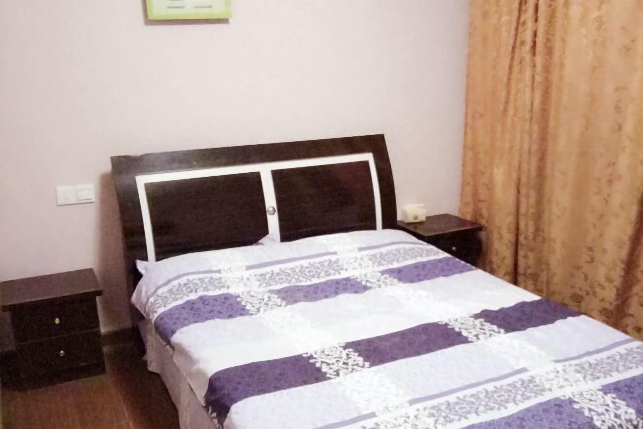 A single bed with a wooden headboard, a patterned bedspread, two bedside tables, and a curtain on the right.