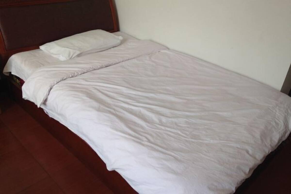 A single bed with a wooden headboard and white bedding in a room with a tiled floor.