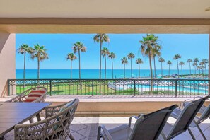 A balcony with wicker furniture, a view of the ocean, palm trees, and a pool.