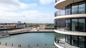 Un bâtiment moderne offrant une vue sur le front de mer, doté d’un balcon circulaire avec des garde-corps noirs.