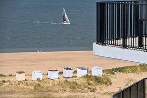 Una playa con un velero, un edificio blanco con barandilla negra y varias estructuras blancas sobre la arena.