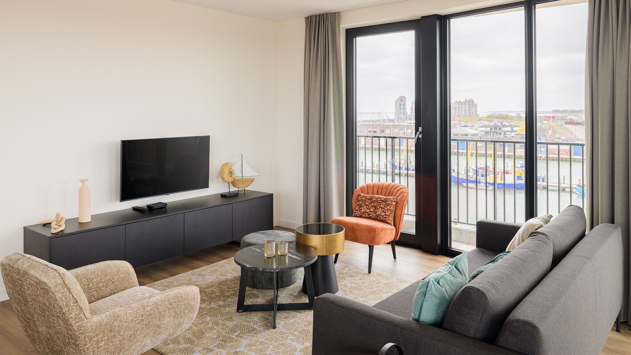 En moderne stue med et fladskærms-tv, en sofa, en lænestol og et spisebord.