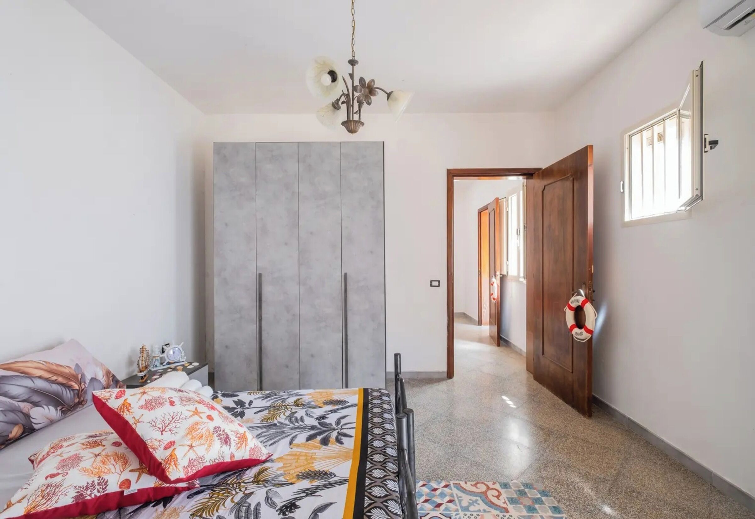 A bedroom with a bed, a wardrobe, a chandelier, and a hallway leading to another room.