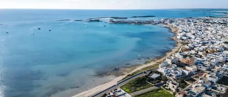 An aerial view of a coastal town with a beach, clear blue waters, and densely packed white buildings.