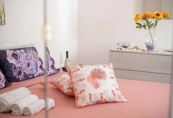 A neatly made bed with floral pillows, a vase with sunflowers, and a dresser with decorative items. - Chill e Relax Sul Mare (Nardò)