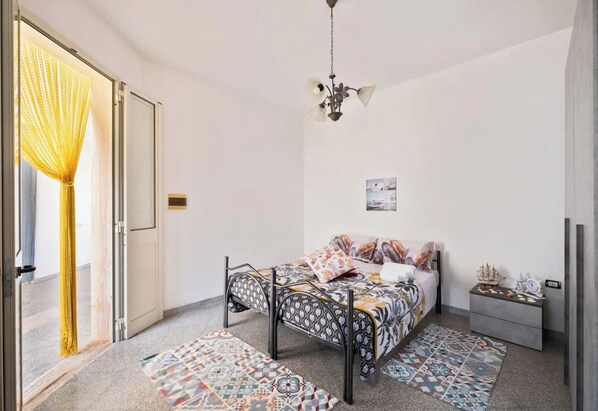 Un dormitorio con una cama, una mesita de noche, una lámpara colgante y una alfombra estampada.