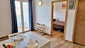 Ein Essbereich mit einem Tisch für zwei Personen, einem Stuhl, einer kleinen Ablage mit Tassen und einer Tür zum Schlafzimmer.